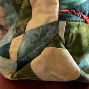 Op de afbeelding: Close-up van een groene en witte patchwork stof met witte stiksels. De stof is gevouwen en heeft een textuur.