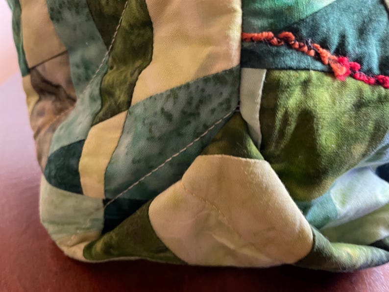 Op de afbeelding: Close-up van een groene en witte patchwork stof met witte stiksels. De stof is gevouwen en heeft een textuur.