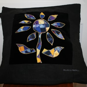 Op de afbeelding: Een zwart fluwelen kussen met een kleurrijk patchwork bloemenontwerp. Het kussen heeft een zwarte rand en de tekst "Made by HeoNa." is geborduurd in de rechterbenedenhoek.