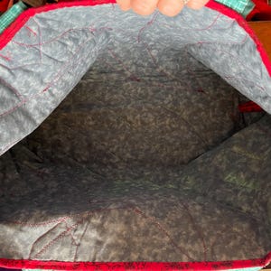 Op de afbeelding: De binnenkant van een rode en witte gewatteerde tote bag met een grijze en witte geprinte voering. De tas is leeg.