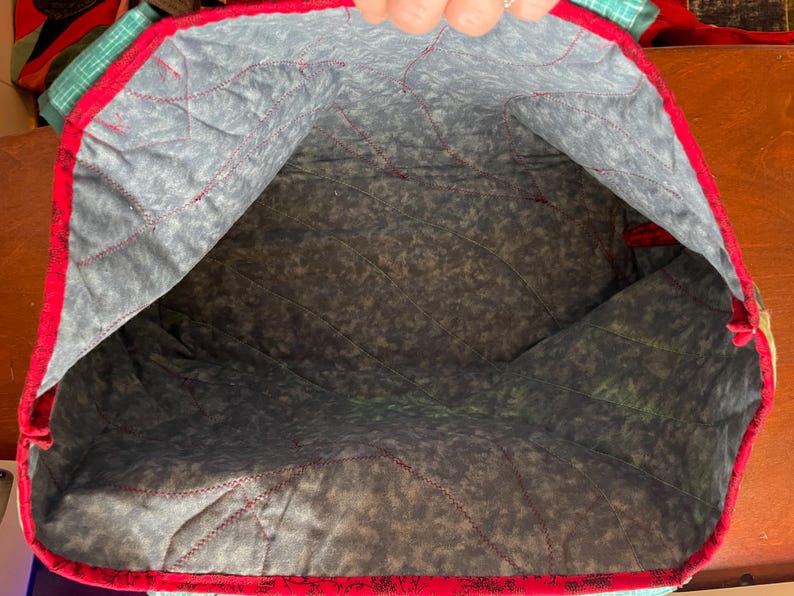 Op de afbeelding: De binnenkant van een rode en witte gewatteerde tote bag met een grijze en witte geprinte voering. De tas is leeg.