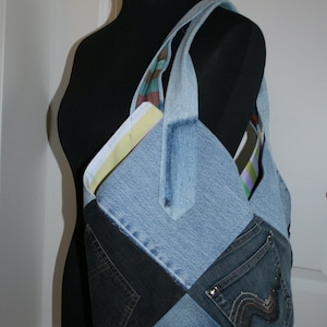 Könnte beinhalten: Eine Denim-Tragetasche aus recycelten Jeans. Die Tasche hat ein Patchwork-Design mit verschiedenen Blautönen und schwarzem Denim. Die Tasche hat eine große Tasche auf der Vorderseite und eine kleinere Tasche auf der Rückseite.
