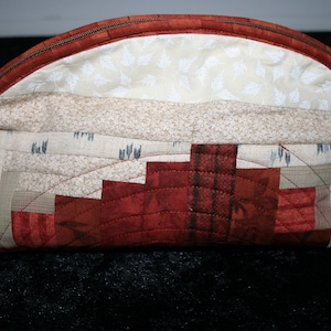 May include: A brown and beige quilted fabric pouch with a zipper closure. The pouch is decorated with a geometric pattern of brown and beige squares.