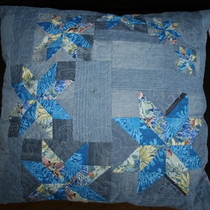 May include: A blue denim cushion with a patchwork design featuring multiple blue and white star-shaped patterns. The cushion is quilted and has a soft, comfortable texture.
