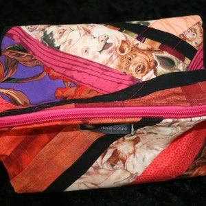 Puede incluir: Una bolsa de cremallera rosa con un diseño de patchwork que presenta una variedad de telas, incluyendo rojo, negro y blanco. La bolsa está decorada con un patrón de cerdos y tiene una etiqueta que dice "Heidi & Anj".