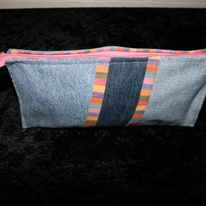 Könnte beinhalten: Eine blaue Jeans-Reißverschlusstasche mit einem rosa Reißverschluss und bunten, gestreiften Stoffakzenten.