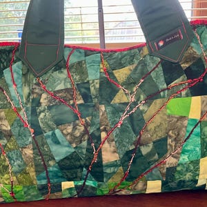 Może przedstawiać: Zielona torba typu tote wykonana z patchworku z czerwonymi szwami i zielonym uchwytem z tkaniny. Torba ma etykietę z napisem "Made in Delft".