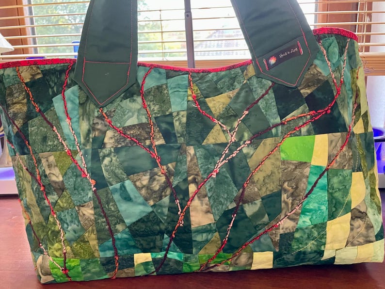 Op de afbeelding: Een groene patchwork tote bag met rode stiksels en een groene stoffen handvat. De tas heeft een label met de tekst "Made in Delft".