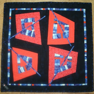 May include: A quilt with a geometric design featuring red, blue and white squares and rectangles. The quilt is made of fabric with a floral pattern.