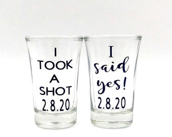 Könnte beinhalten: Zwei klare Schnapsgläser aus Glas mit schwarzer Beschriftung. Das linke Glas trägt den Text I TOOK A SHOT 2.8.20 in Blockschrift. Das rechte Glas trägt den Text I said yes! 2.8.20 in einer Kombination aus Block- und Schreibschrift.