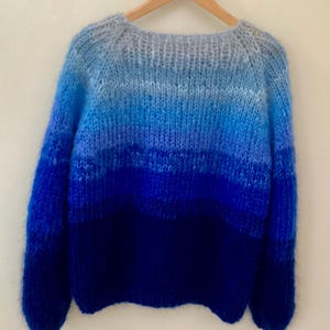 May include: A blue ombre knit jumper with a round neckline and long sleeves.