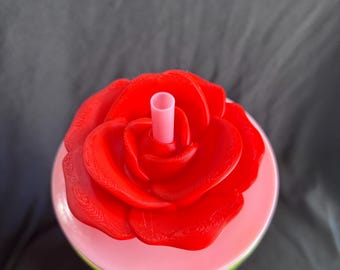 May include: A red rose-shaped lid tops a tumbler with a pink and green gradient. A pink straw extends from the center of the rose. The tumbler is set against a dark gray background.