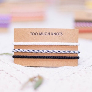 Op de afbeelding: Een close-up van drie verschillende gekleurde koorden die om een kartonnen kaart zijn gewikkeld. De kaart heeft de tekst "Too Much Knots" erop gedrukt.