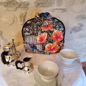 Può includere: Un servizio da tè con una teiera decorativa con un motivo a gabbia per uccelli e accenti floreali arancioni. Il set include una teiera d'argento, panna, due tazze e piattini. La teiera è alta circa 30 cm.