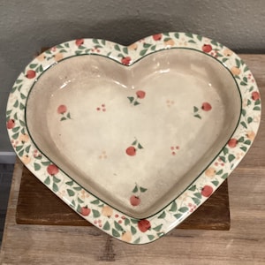 May include: A heart-shaped ceramic baking dish with a white glaze and a green, red, and yellow floral pattern.