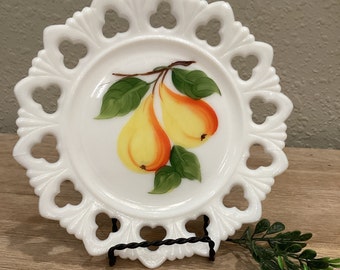 May include: White milk glass plate with a scalloped edge and a pear design. The plate has a delicate, lacy look and features two pears with green leaves painted on the surface.