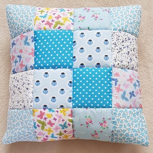 May include: A patchwork cushion with a blue background and various patterns, including butterflies, ladybirds, and polka dots.