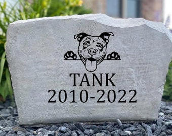 May include: A gray stone memorial with a black silhouette of a dog's head peeking over the top. The stone is engraved with the words "TANK 2010-2022".