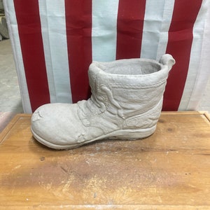 May include: A gray concrete boot planter with a textured surface. The boot is sitting on a wooden table.