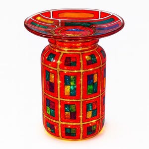 May include: A decorative red glass candle holder with a wide, shallow top and a cylindrical base. The base is adorned with a grid pattern of colorful squares, outlined in gold. The top also features a colorful design.