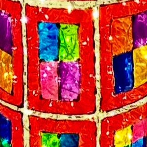 May include: A decorative, spherical object with a red, grid-like pattern. Each grid square contains four smaller squares of various colors, including blue, green, pink, and yellow. The object has a textured appearance.