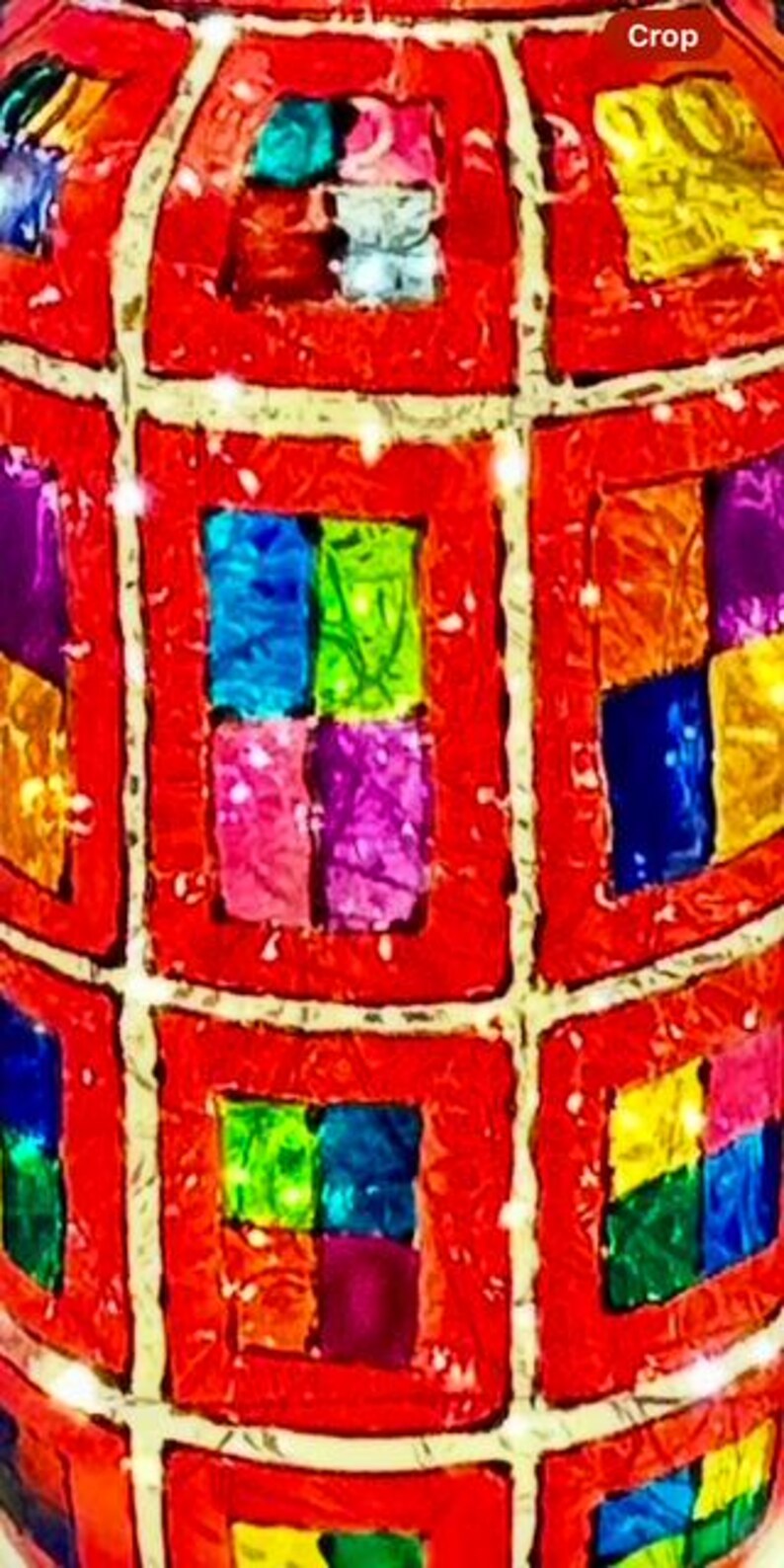 May include: A decorative, spherical object with a red, grid-like pattern. Each grid square contains four smaller squares of various colors, including blue, green, pink, and yellow. The object has a textured appearance.