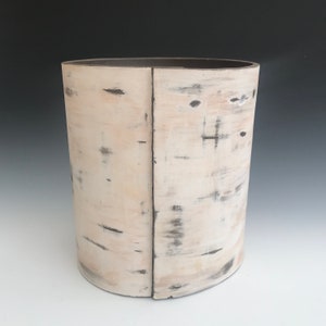 May include: A white ceramic cylinder vase with a distressed, wood-like finish. The vase has a subtle, uneven texture and a dark brown rim.