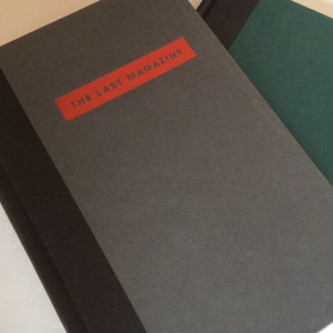 May include: A stack of books with a gray cover and a red rectangular label that reads "THE LAST MAGAZINE". The spine is black. Another book with a green cover is partially visible.