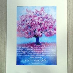 May include: A framed print featuring a watercolour painting of a pink flowering tree. The print includes a quote from 1 Corinthians 13:4-8 about love being patient, kind, and never failing.