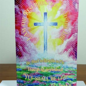 May include: A watercolour painting of a cross with a rainbow background. The text "I AM THE RESURRECTION AND THE LIFE" is written in a circle around the cross. The text "He that believeth in Me Though he were dead YET SHALL HE LIVE John II:25" is written below the cross.
