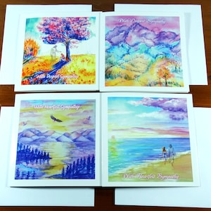 Könnte beinhalten: Vier Beileidskarten mit Aquarell-Landschaftsbildern. Jede Karte zeigt eine andere Szene: einen Baum mit Figuren, Berge, einen See mit einem Vogel und einen Strand mit Figuren. Jede Karte hat einen weißen Rand und wird mit einem weißen Umschlag geliefert.