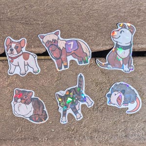 May include: A collection of six animal stickers. The stickers feature a bulldog, a pony with a number 7 on its saddle, a dog, a cat, another cat, and an opossum. The stickers have a holographic finish.