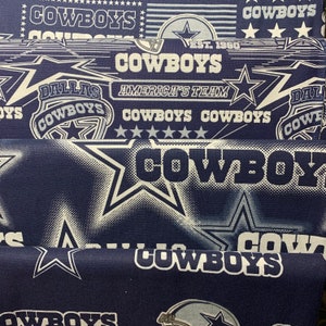 May include: A blue fabric with a white star pattern and the words "Dallas Cowboys" and "America's Team" repeated throughout. The fabric also features a white star with a blue outline and the word "Cowboys" in white.