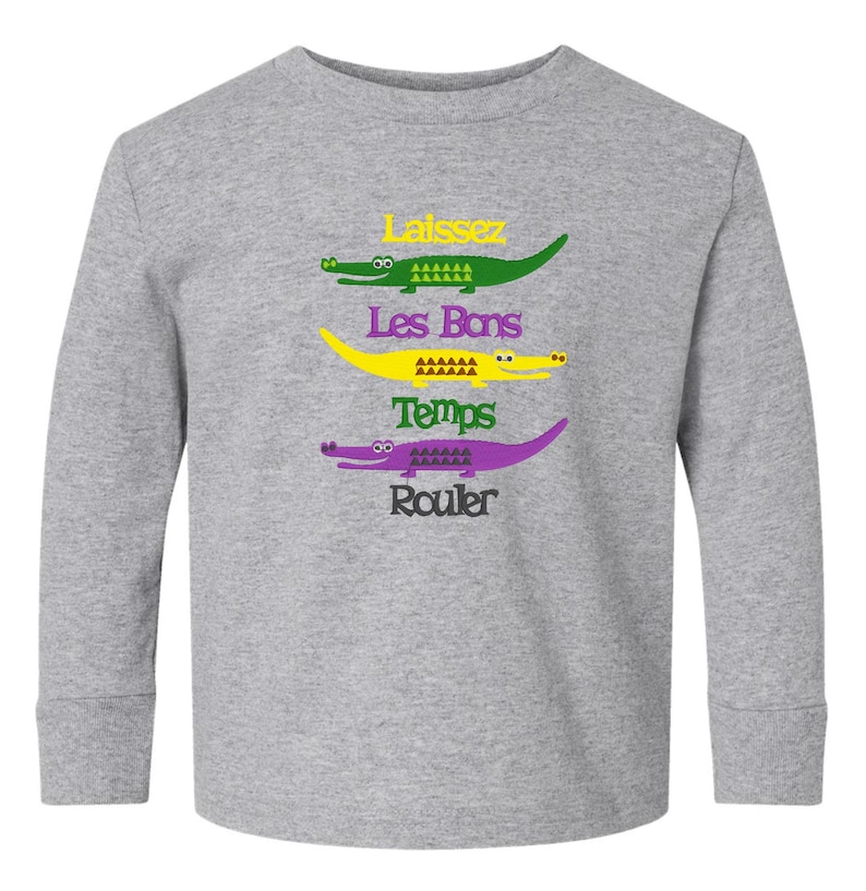 Puede incluir: Una camiseta gris de manga larga con un gr&aacute;fico de cuatro caimanes y el texto "Laissez Les Bons Temps Rouler" en amarillo, verde y morado.