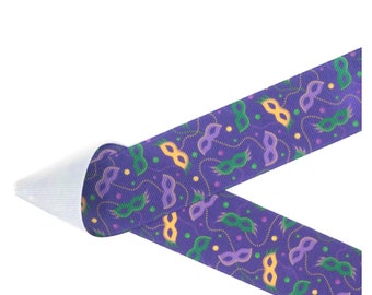 May include: Purple ribbon with a repeating pattern of Mardi Gras masks in yellow, green, and purple. The ribbon is folded over, revealing a white, textured underside. The design includes dotted lines.
