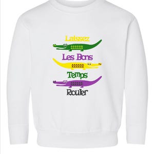 Puede incluir: Sudadera blanca con un dise&ntilde;o de cocodrilo verde, amarillo y morado. El texto "Laissez Les Bons Temps Rouler" est&aacute; impreso en la sudadera.