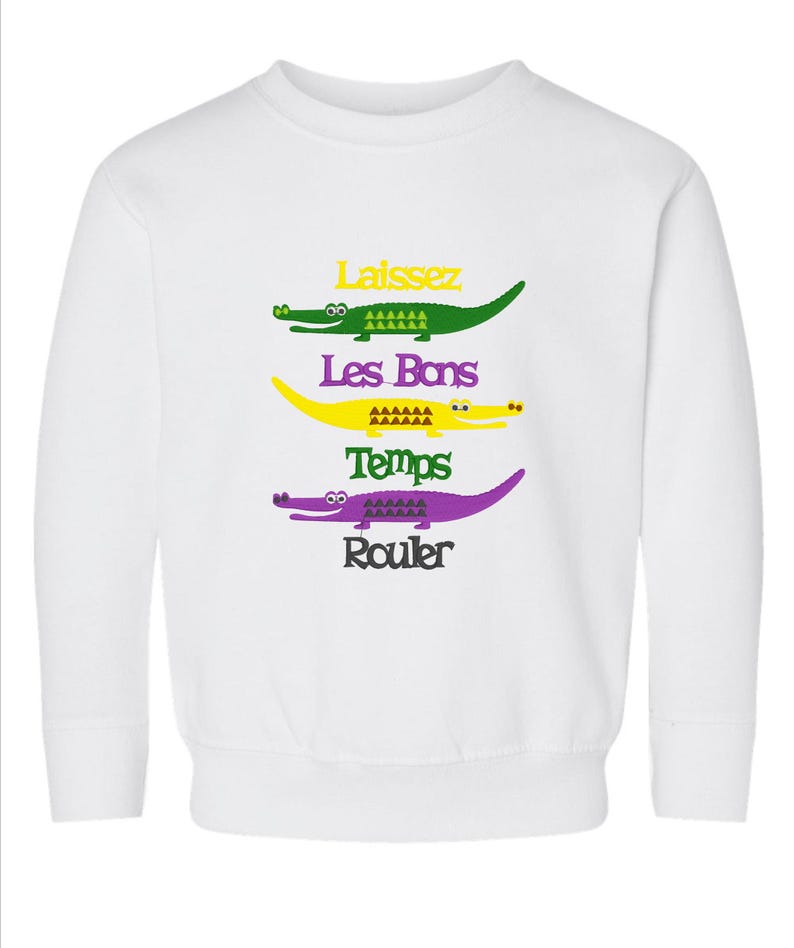 Puede incluir: Sudadera blanca con un dise&ntilde;o de cocodrilo verde, amarillo y morado. El texto "Laissez Les Bons Temps Rouler" est&aacute; impreso en la sudadera.