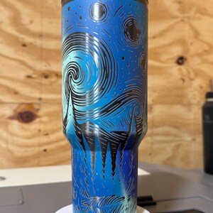 Puede incluir: Un vaso de acero inoxidable con tapa y pajita negras. El vaso presenta un dise&ntilde;o azul y negro inspirado en la pintura "La noche estrellada" de Van Gogh. El dise&ntilde;o envuelve todo el vaso, creando un aspecto &uacute;nico y art&iacute;stico.