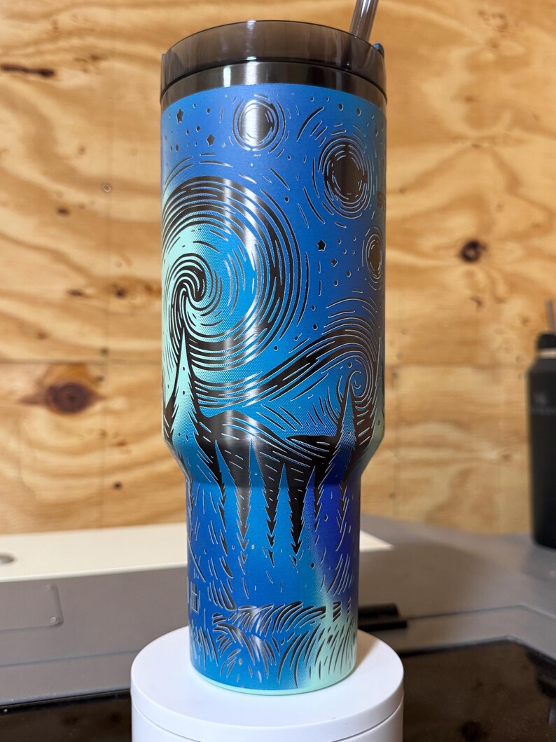 Puede incluir: Un vaso de acero inoxidable con tapa y pajita negras. El vaso presenta un dise&ntilde;o azul y negro inspirado en la pintura "La noche estrellada" de Van Gogh. El dise&ntilde;o envuelve todo el vaso, creando un aspecto &uacute;nico y art&iacute;stico.