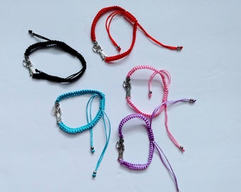 May include: Five colorful braided bracelets with silver angel charms. The bracelets are red, black, turquoise, pink, and purple.