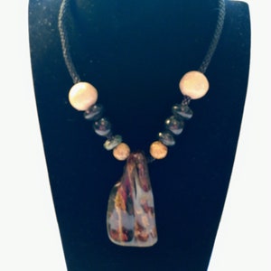 May include: A necklace with a black cord and brown and black beads. The necklace has a large, irregular-shaped pendant made of brown, red, and green glass.
