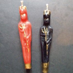 Può includere: Due candele decorative a forma di figure con una corona e un tridente. La candela a sinistra è rossa e la candela a destra è nera.