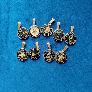 May include: A collection of gold-colored pendants with black circular faces. Each pendant features a different symbol or design, including stars, geometric shapes, and other occult symbols. The pendants are displayed on a blue surface.
