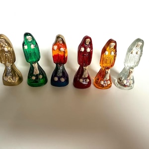 May include: Six small standing figurines of hooded skeletal figures, each featuring a distinct translucent or metallic color including gold, green, orange-red, deep red, amber, and clear, with white skeletal details visible on the front of each.