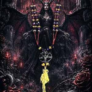May include: A necklace featuring a gold-toned pendant of a figure, suspended from a red cord adorned with purple and gold beads. The necklace includes a circular black charm with a star design, positioned above the gold pendant on the cord.