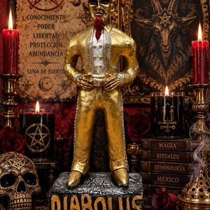 Könnte beinhalten: Eine goldfarbene Figur eines gehörnten Wesens mit rotem Spitzbart, das eine weiße Weste und einen goldenen Anzug trägt und auf einem rechteckigen Sockel mit dem Wort DIABOLUS in goldenen Buchstaben steht. Die Figur hat spitze Ohren und einen ernsten Ausdruck.