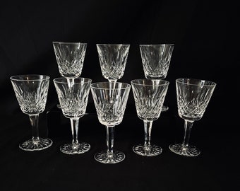 Könnte beinhalten: Eine Sammlung von neun klaren Kristallgläsern, darunter Weingläser und Tumbler. Die Gläser haben ein geschliffenes Design und sind auf einer schwarzen Oberfläche angeordnet. Die Weingläser haben Stiele und runde Basen.