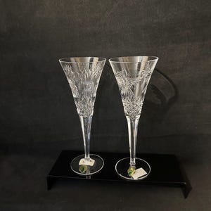 May include: Two clear crystal champagne flutes with a cut glass design. The flutes are on a black surface.