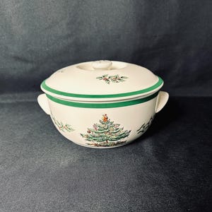 May include: A white ceramic soup bowl with a lid, featuring a green trim and handles. The bowl is decorated with a Christmas tree and holly sprigs. The lid has a small knob and is also decorated with holly sprigs.