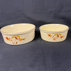 May include: Two cream-colored ceramic ramekins with a ribbed design and a gold trim. Each ramekin features a floral pattern in shades of orange, yellow, and brown. The ramekins are oval and round, perfect for baking and serving individual portions.